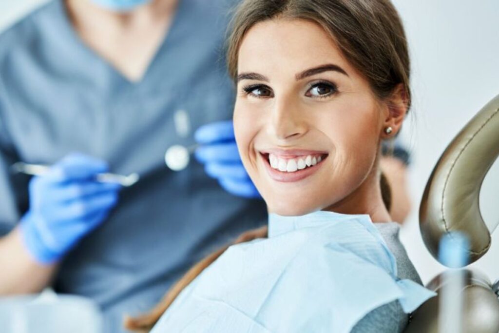 Woman smiling in dental chair with dentist holding tools in background at dental office.